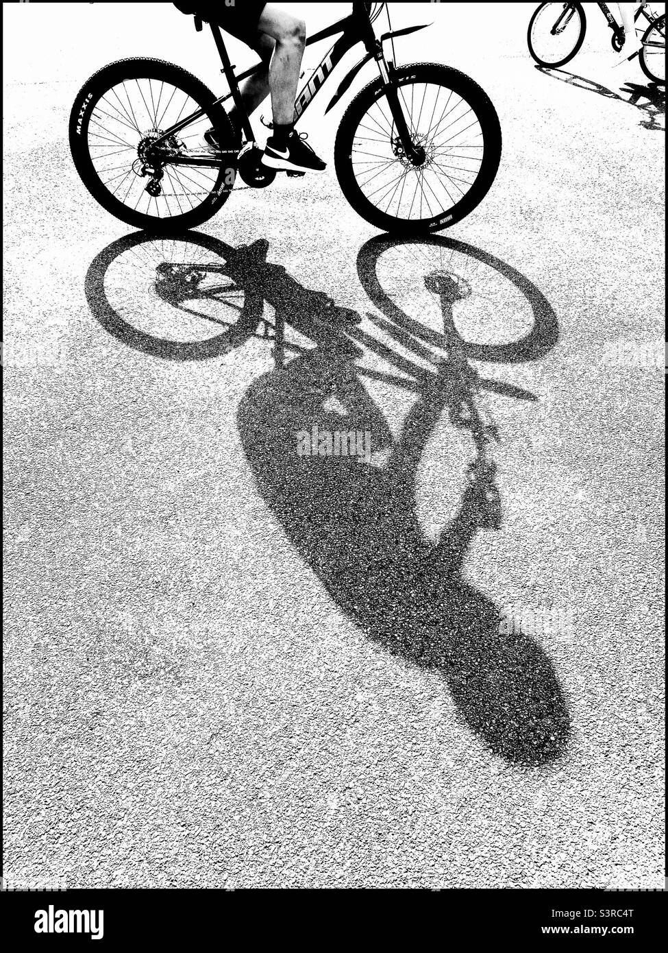A high key image of two children cycling on a bright tarmac surface. Bright sunshine creates interesting shadows. Photo ©️ COLIN HOSKINS. Stock Photo