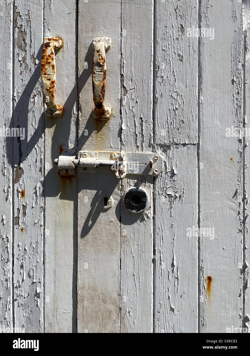 Old wooden door with flaking white paint and rusting handles and lock. Stock Photo