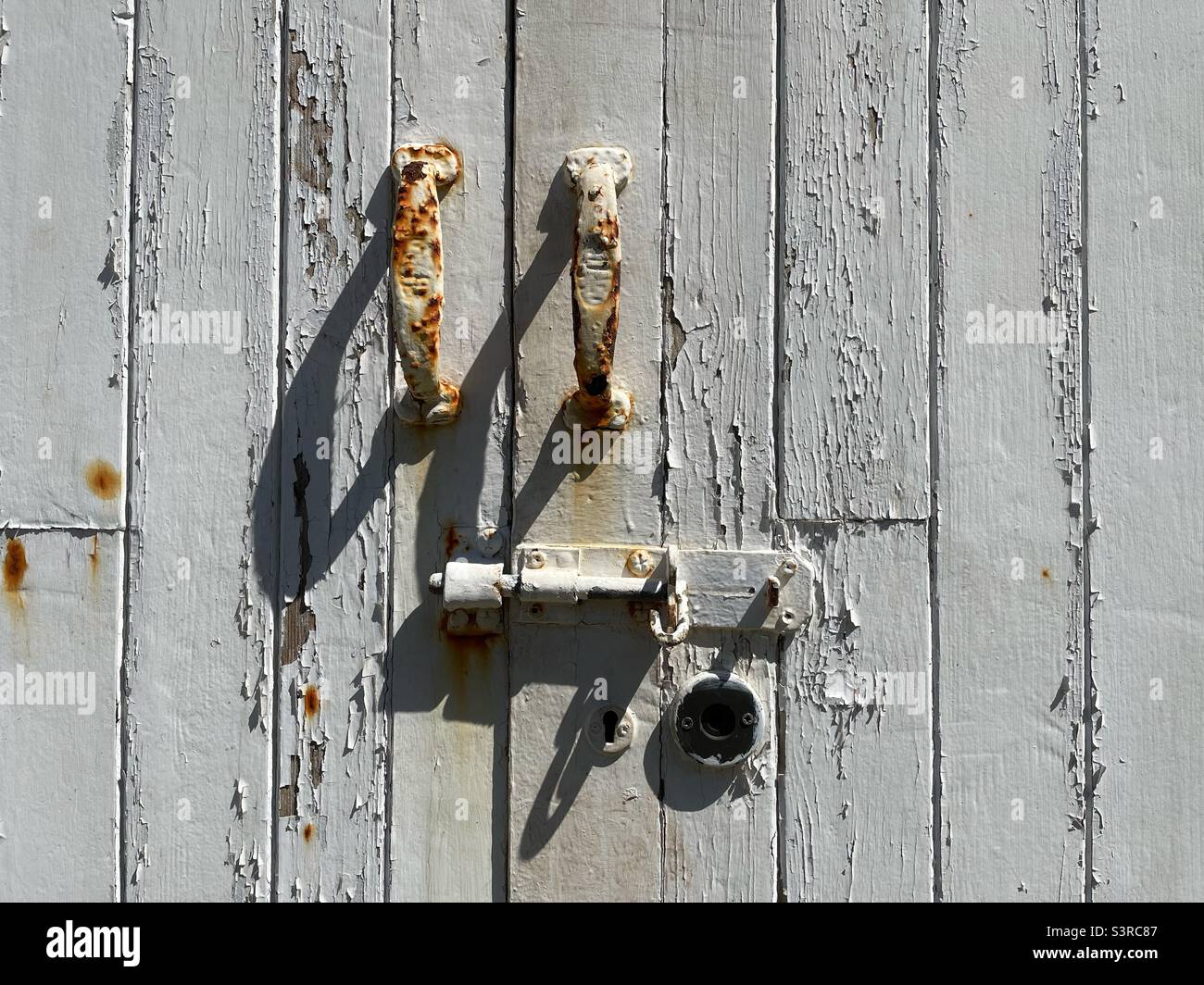 Old wooden door with peeling white paint, rusting handles and bolt. Stock Photo