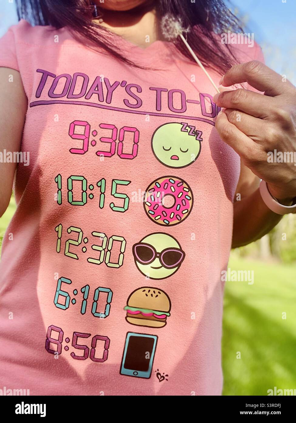 A girl wearing a funny To-Do list TShirt holding a half dandelion poof in her hands. Stock Photo