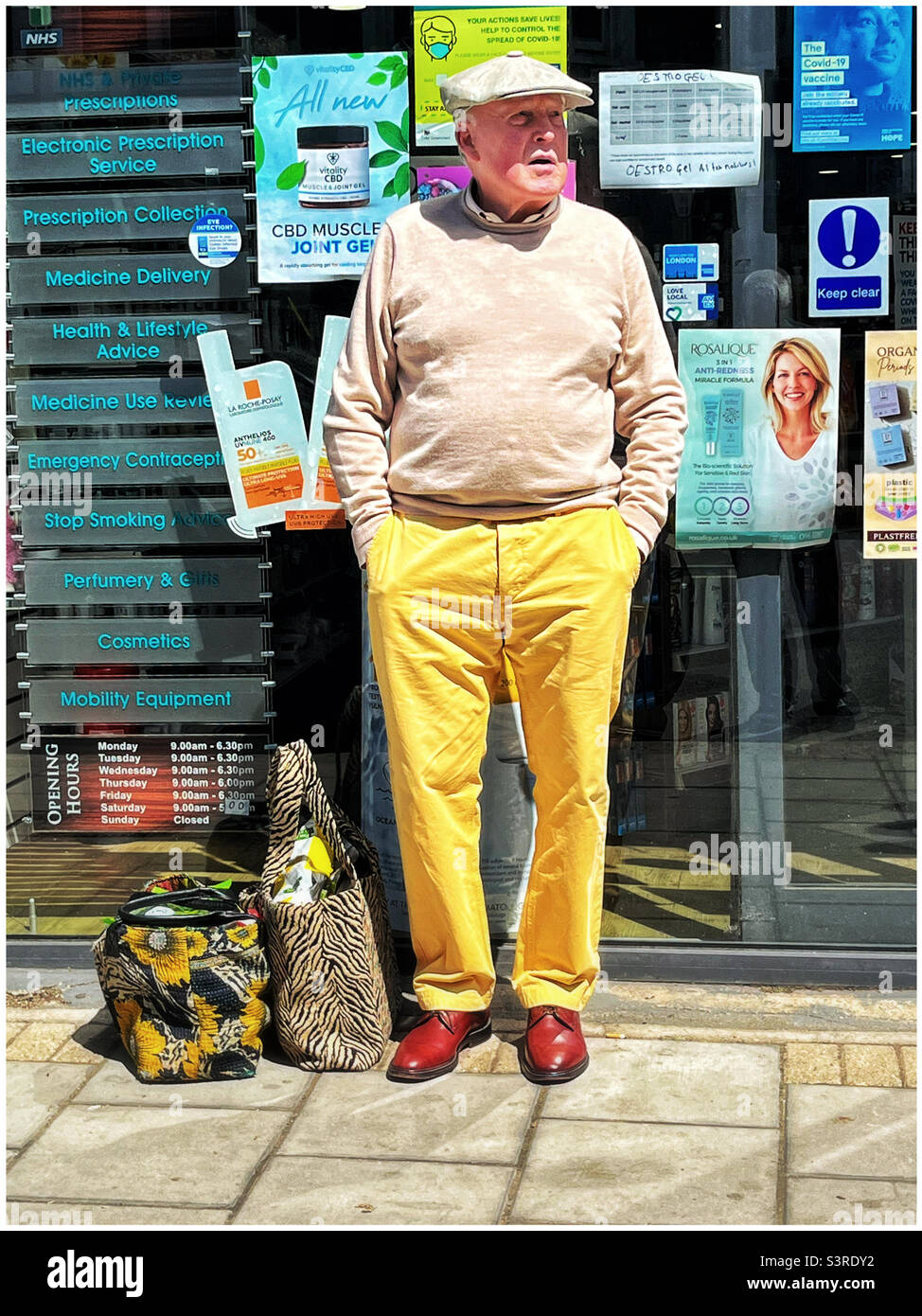 Elderly man dressed in yellow trousers, outside a pharmacy in Muswell Hill, London - Smartphone Captured Stock Image