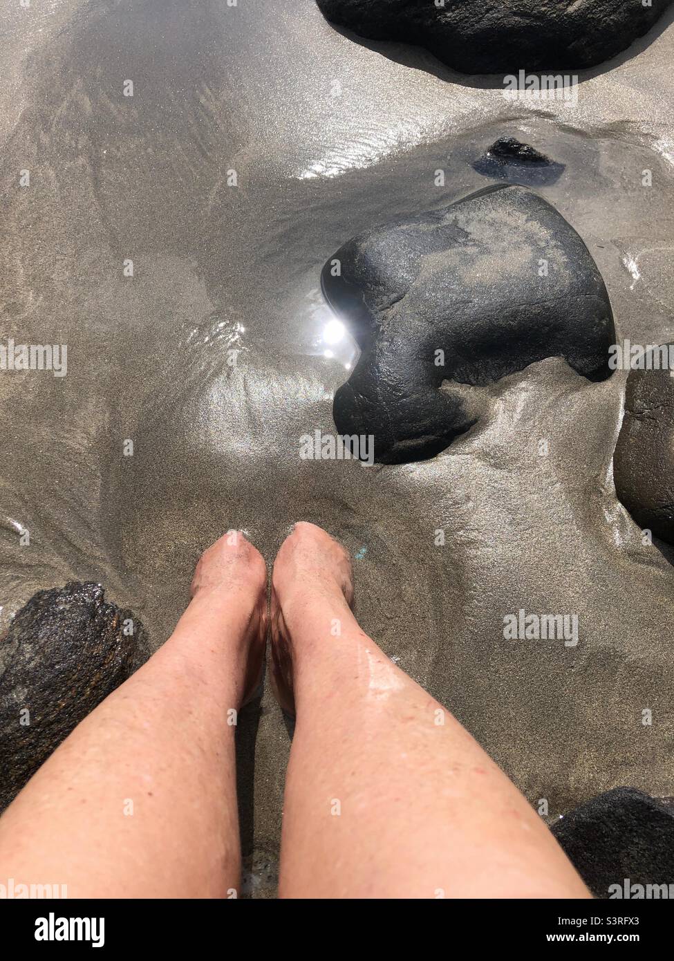A woman’s feet buried in sea mud. Stock Photo