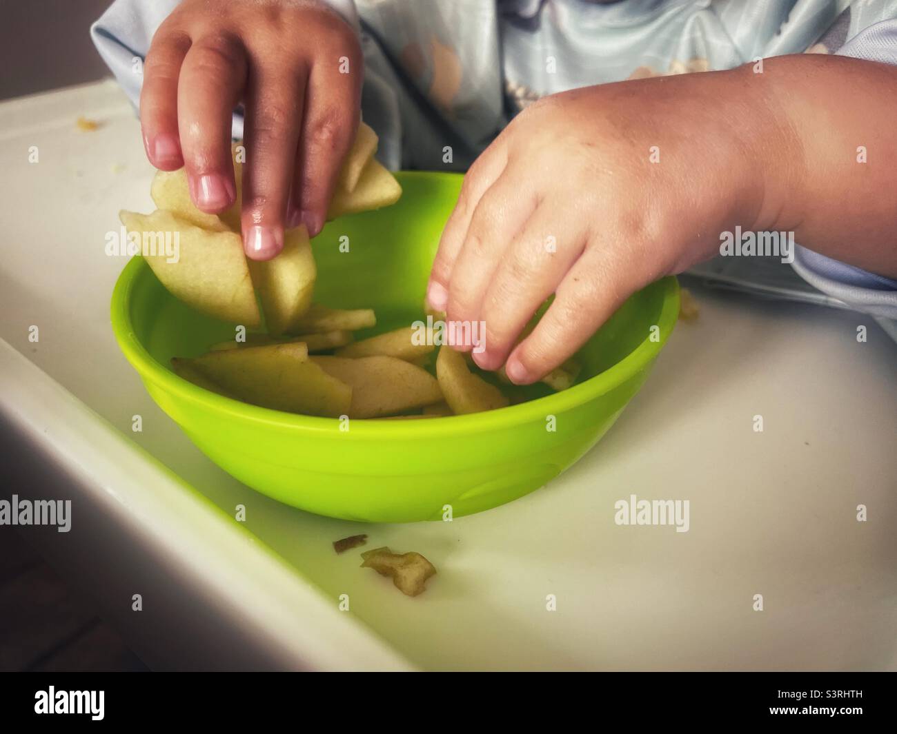 Child eating chopped apple from green bowl - toddler food- finger food- weaning baby- child hands- supper- tea- dinner- high chair Stock Photo