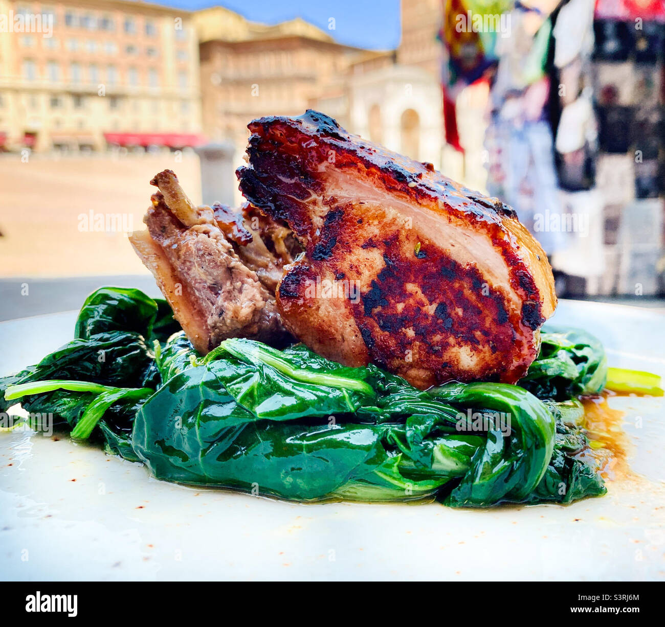 Roasted pork shank on a bed of lettuce with outdoor dining in Siena, Italy Stock Photo