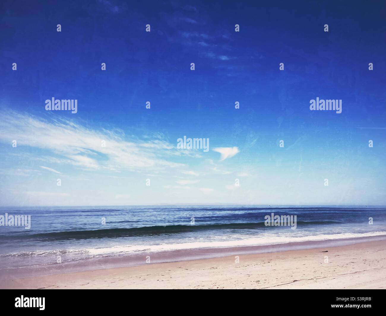 Sandy beach with ocean waves rolling onto shore on a sunny day. - Smartphone Captured Stock Image