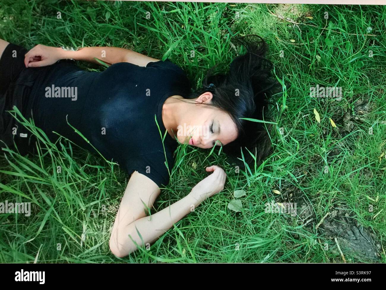 Young woman, sunning herself, on the park lawn, green grass, creek, sunny day, black top, shorts Stock Photo