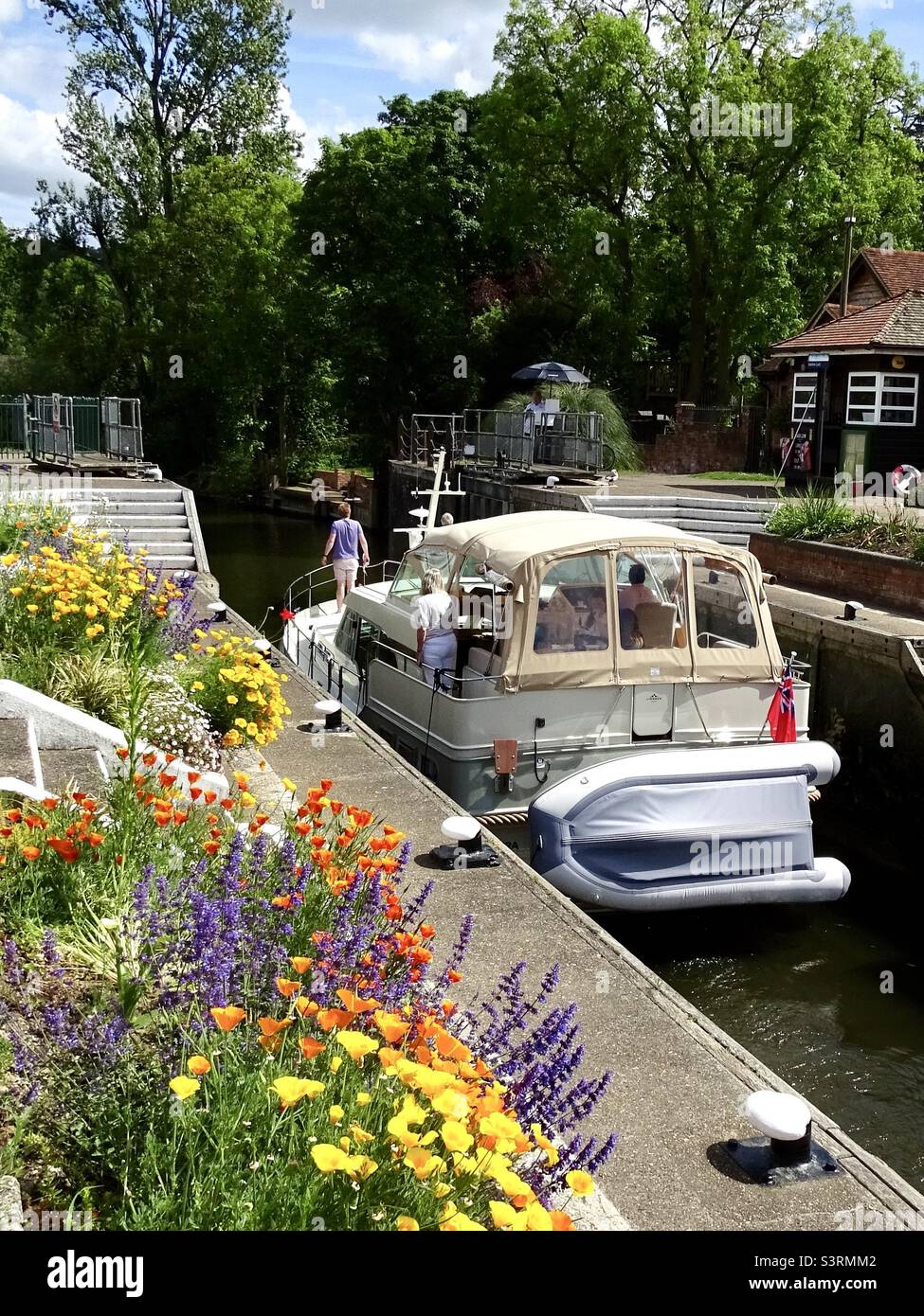 A boat passing through Marlow lock with beautiful flowers on the quayside. Stock Photo