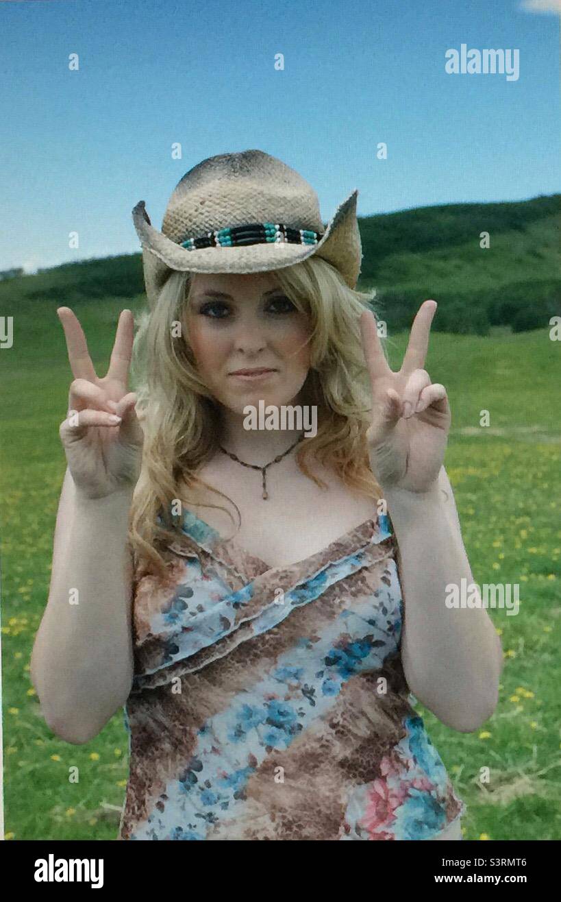 Girl with a straw hat, hi, hand signal, keeping fit, exercise, active, activity, action, 20’s, green field, woman, female, blonde, fun , pretty,pleasant , sunny day , hills, prairie, hat Stock Photo