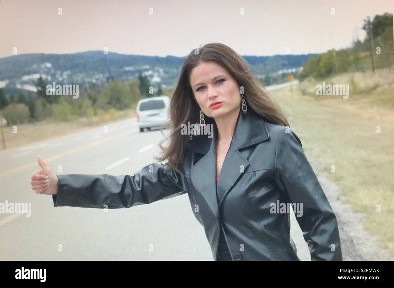 Hitch hiker, woman, pretty girl, Windy day,  brunette, thumbing a ride, thumbs up, flowing hair, road, need a ride Stock Photo