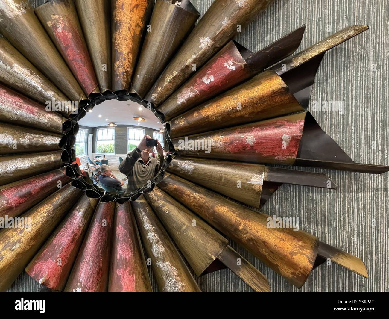 A convex mirror with an elaborate surround reflects the lounge of a seaside hotel in North Wales - Smartphone Captured Stock Image