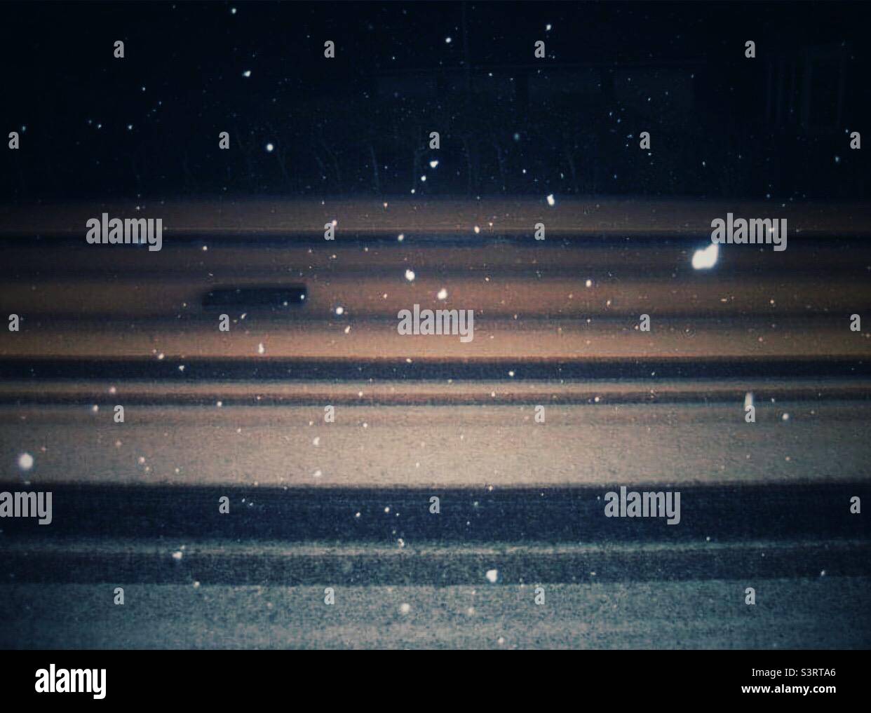 Falling snowflakes and tyre tread marks on an icy road Stock Photo
