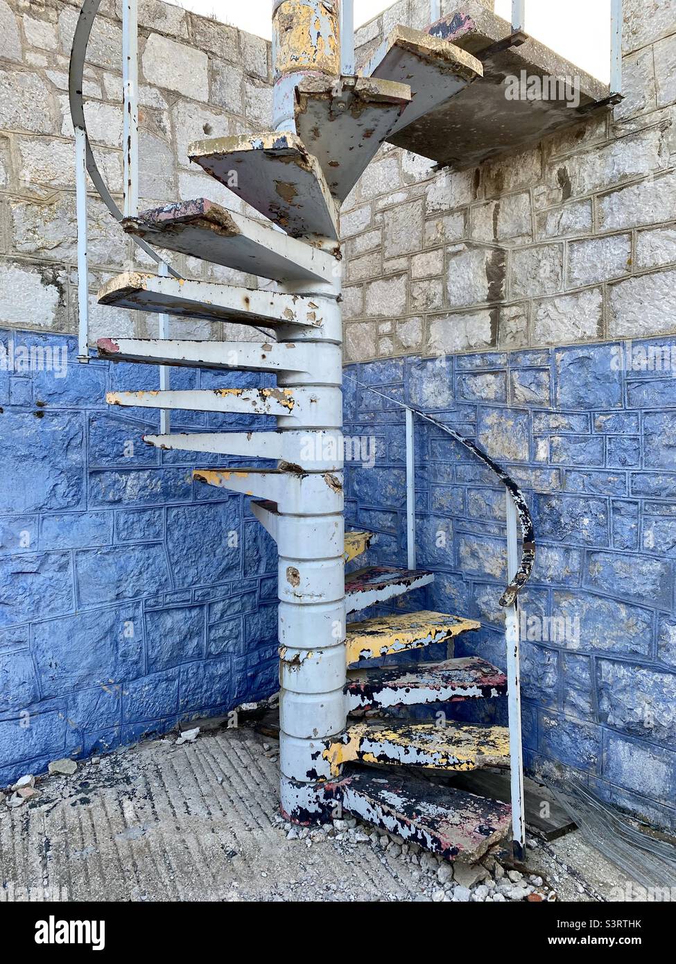 Old concrete spiral staircase with lots of layers of coloured peeling paint Stock Photo