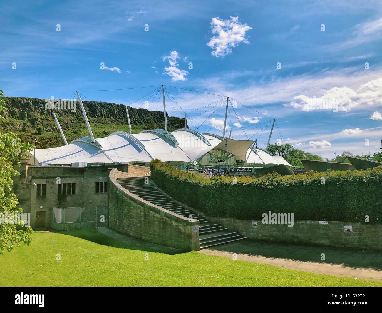 Dynamic Earth, Edinburgh, Scotland on a sunny day with blue sky. State-of-the-art family attraction taking visitors through history from the Big Bang to modern day. Salisbury Crags in the background. Stock Photo