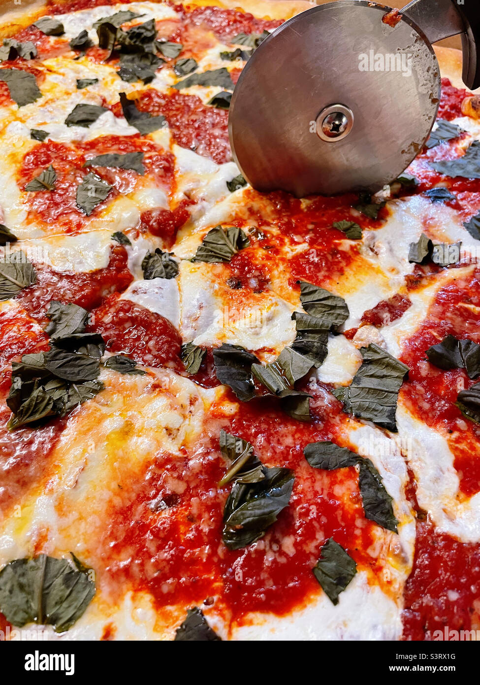 Pizza cutting wheel slicing a margherita pizza fresh from the oven, 2022, USA - Smartphone Captured Stock Image
