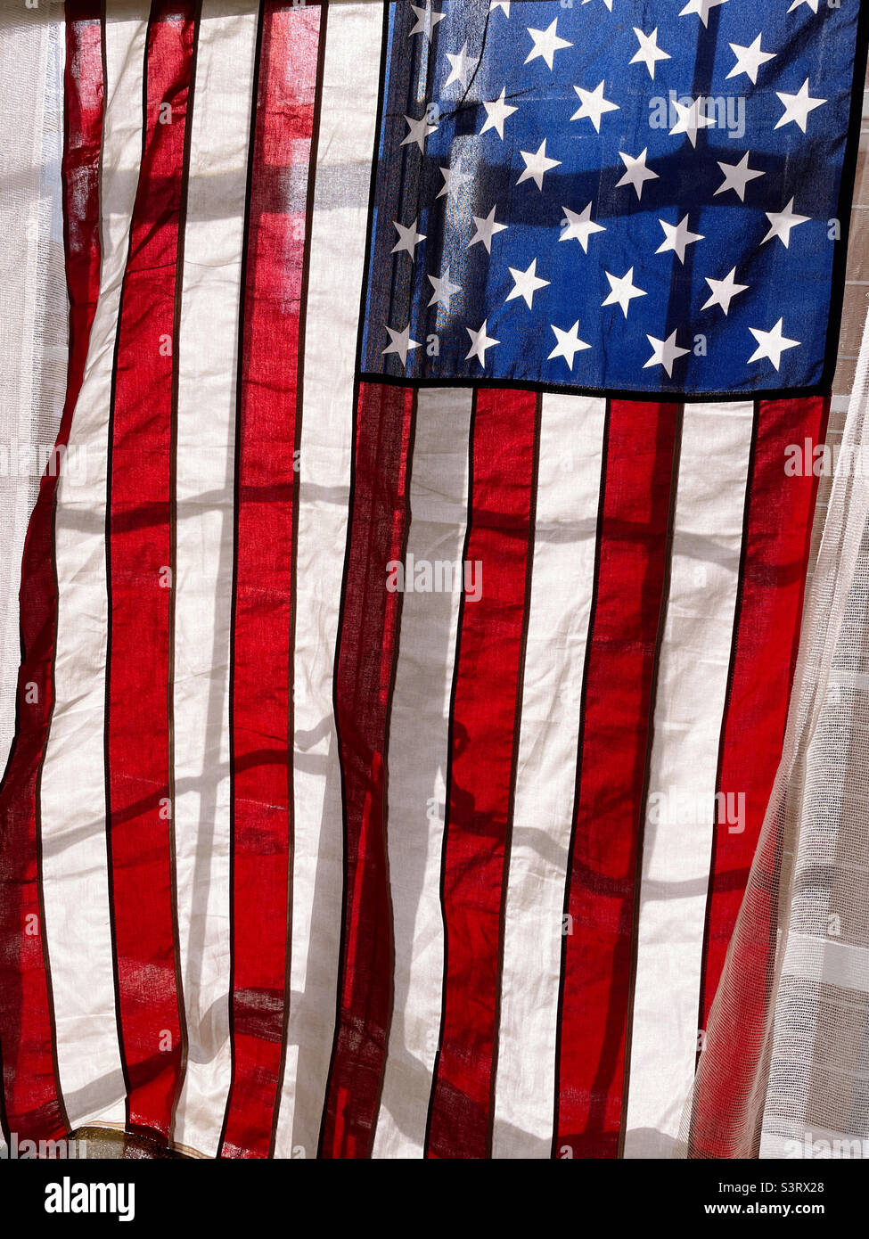 An American flag on display in a New York City apartment in a casement window on a sunny afternoon, 2022, USA - Smartphone Captured Stock Image