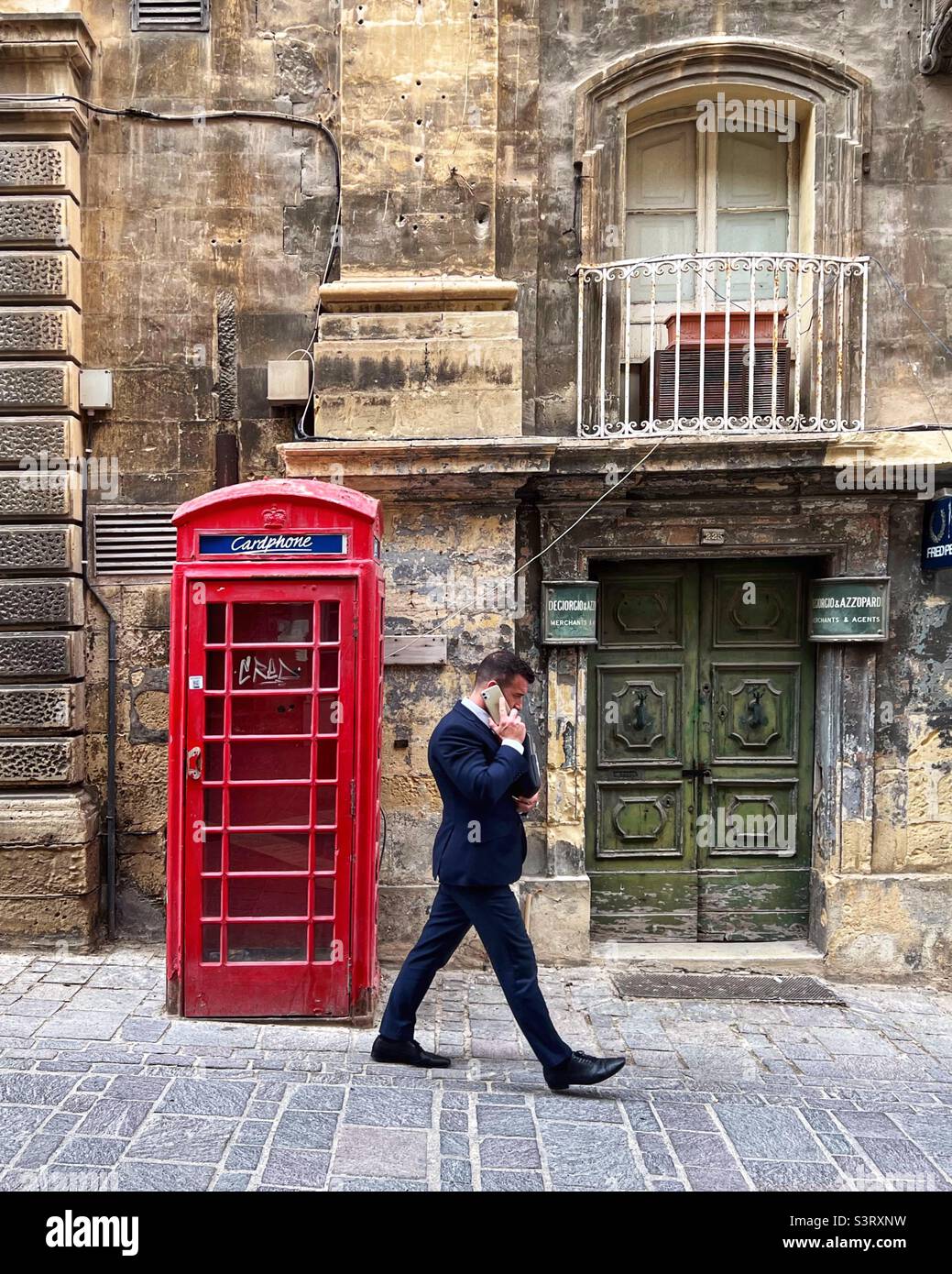 Red public phone box and businessman on mobile phone, Valletta, Malta - Smartphone Captured Stock Image