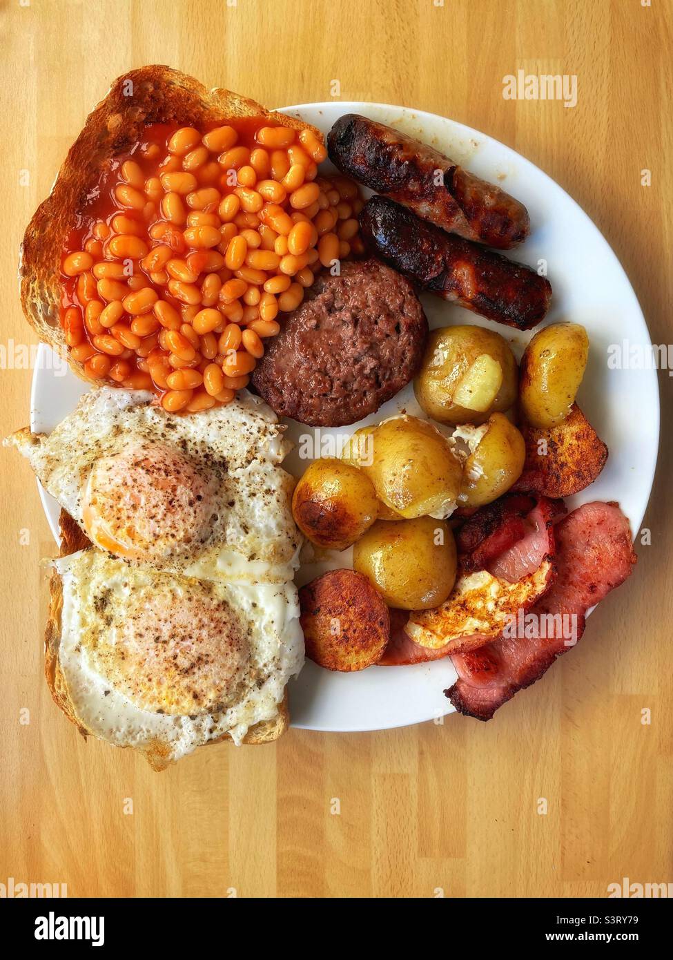 Monster brunch- eggs, sausages, bacon, potatoes, beans, toast and a burger. Stock Photo