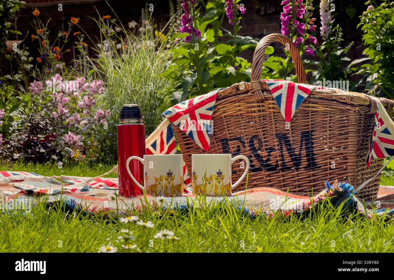 Wicker picnic hamper on blanket outdoors in garden with two celebration jubilee mugs and a red flask - Smartphone Captured Stock Image