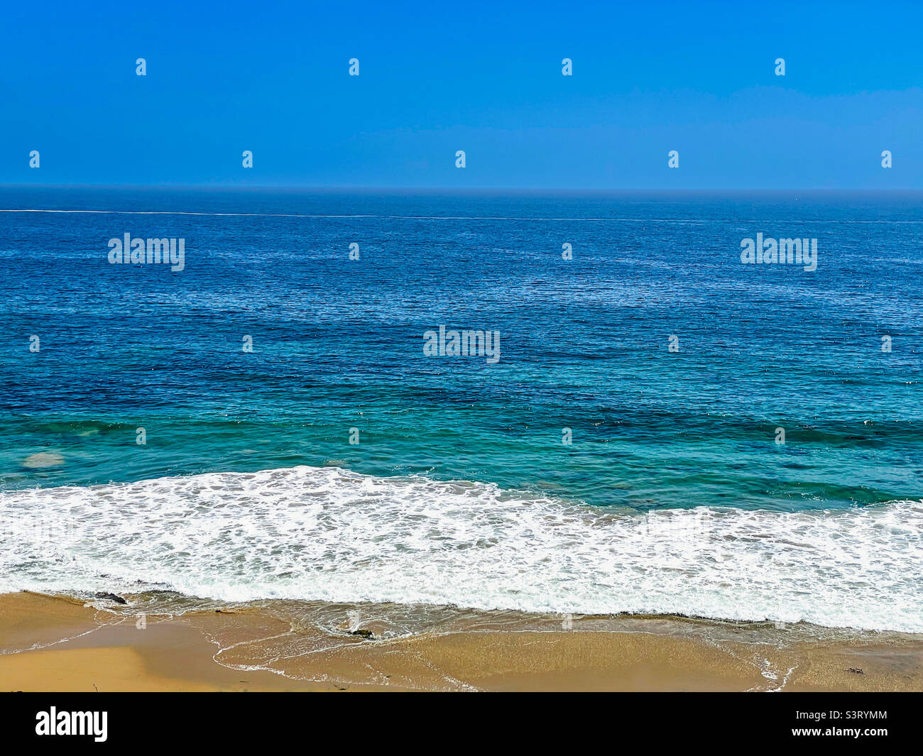 Vibrant seascape of waves washing up onto sandy beach on a sunny hot day. - Smartphone Captured Stock Image