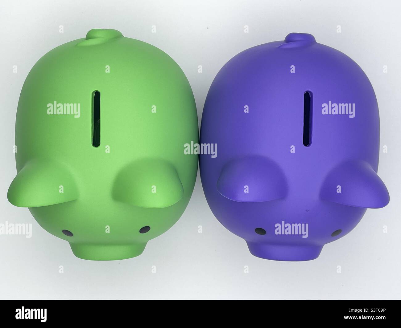 Two differently colored children’s piggy banks, purple and lime green, sitting side by side, as seen from above. - Smartphone Captured Stock Image