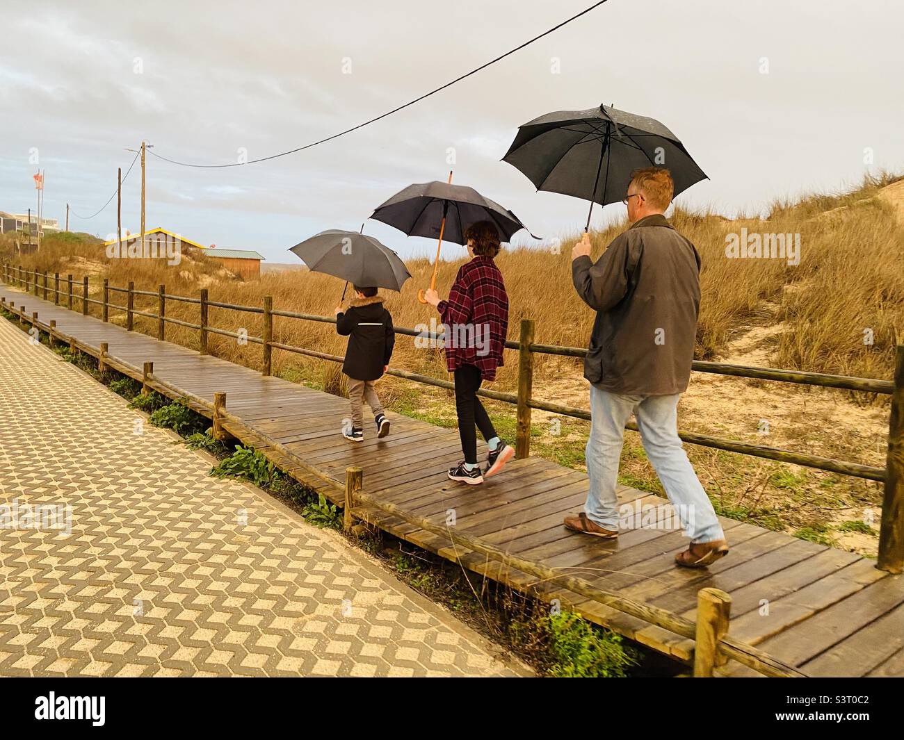 Family walking along a boardwalk in the rain all with umbrellas Stock Photo