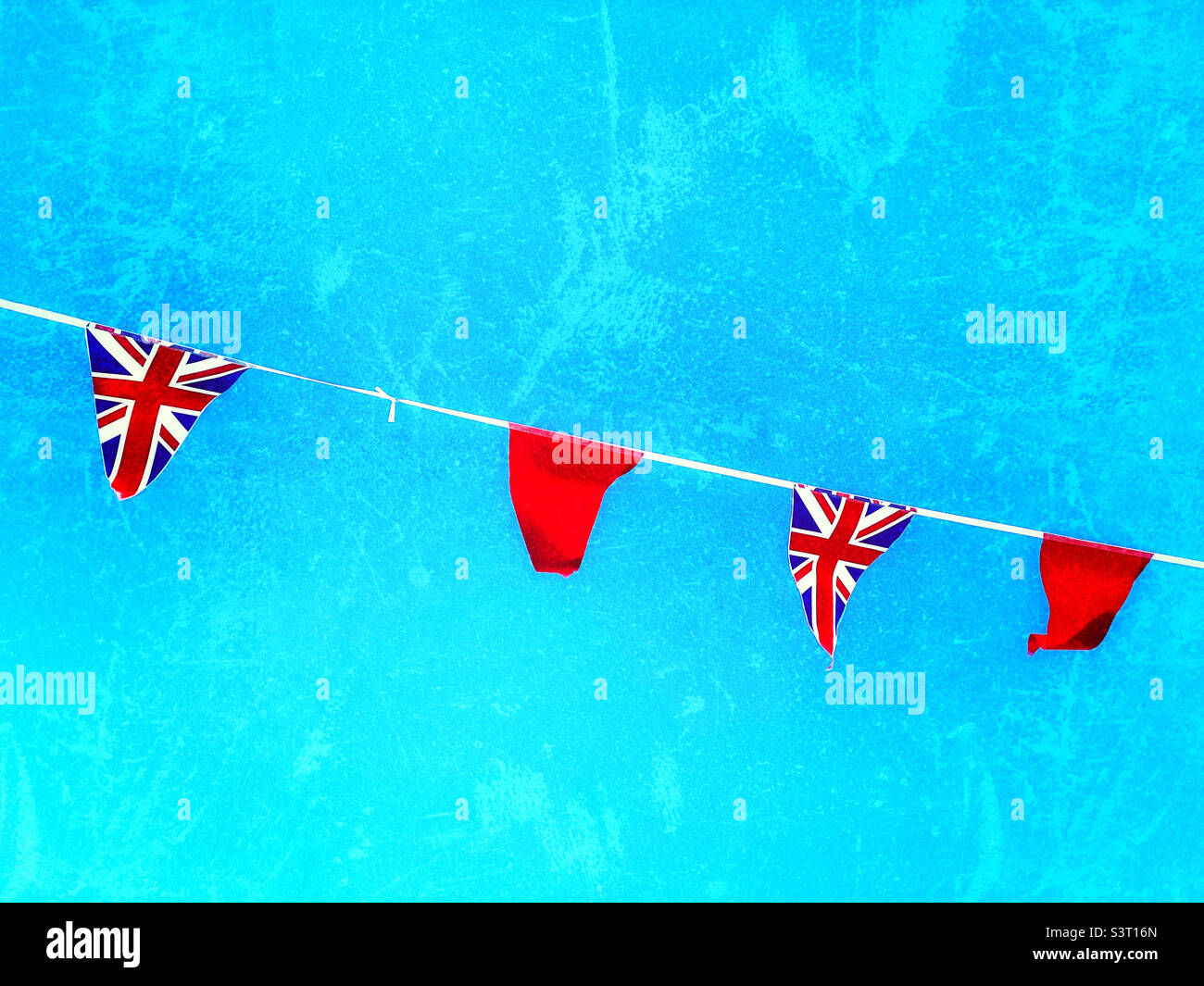 Union Jack Bunting. Red flags in a line of Union Jack flags. Blue skies in a British summer. A small celebration of the Queen’s Platinum Jubilee. Photo ©️ COLIN HOSKINS. Stock Photo