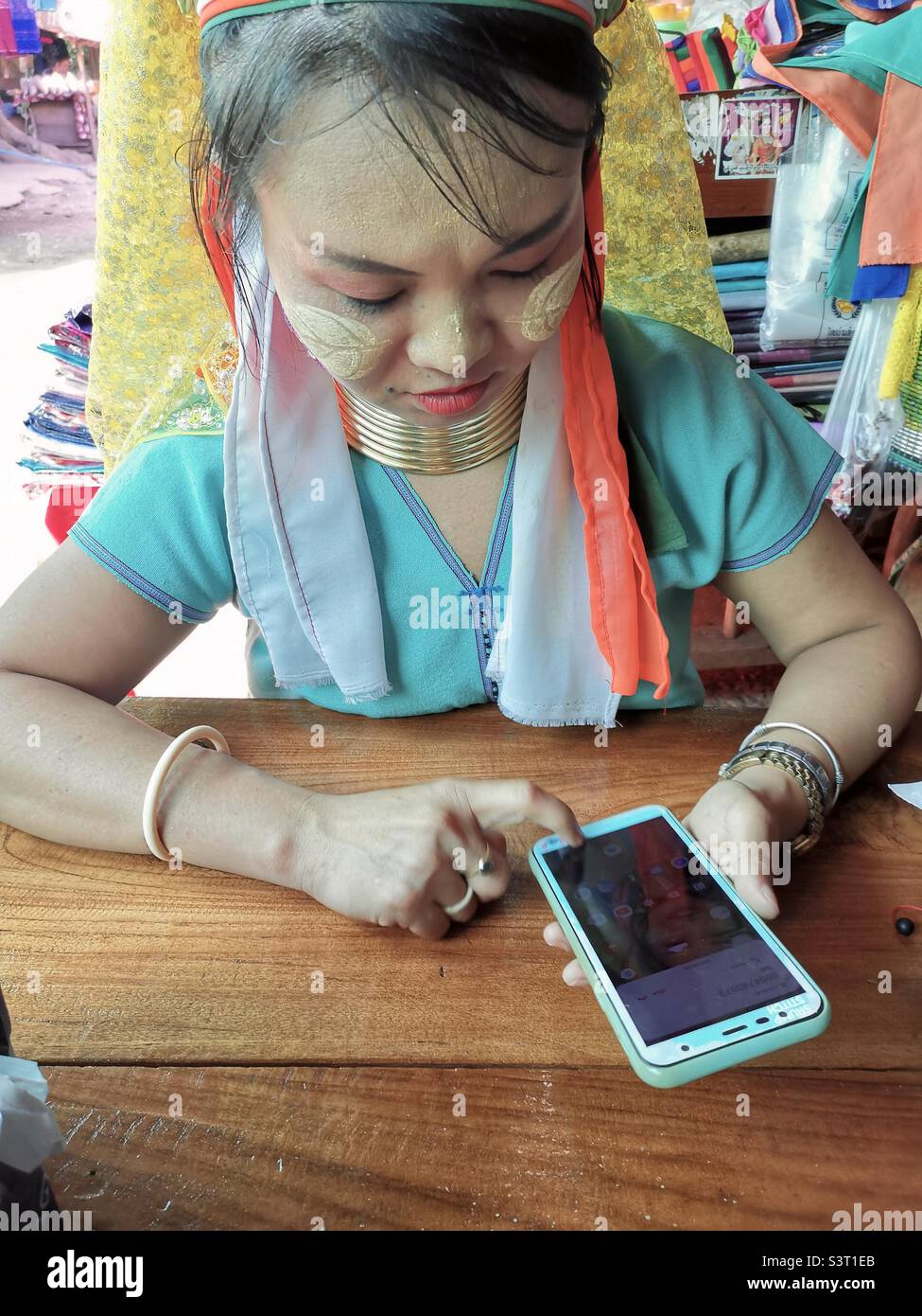 A Padaung / Red Karen long neck woman using her smartphone in Mae Hong Song province in Thailand. - Smartphone Captured Stock Image