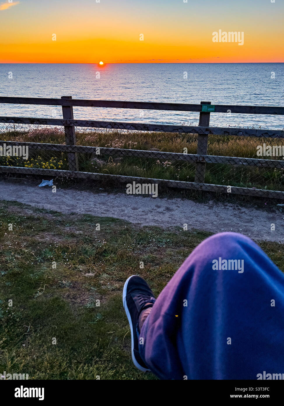 Man sitting on cliff top watching sun setting at Perranporth, Cornwall, UK - Smartphone Captured Stock Image