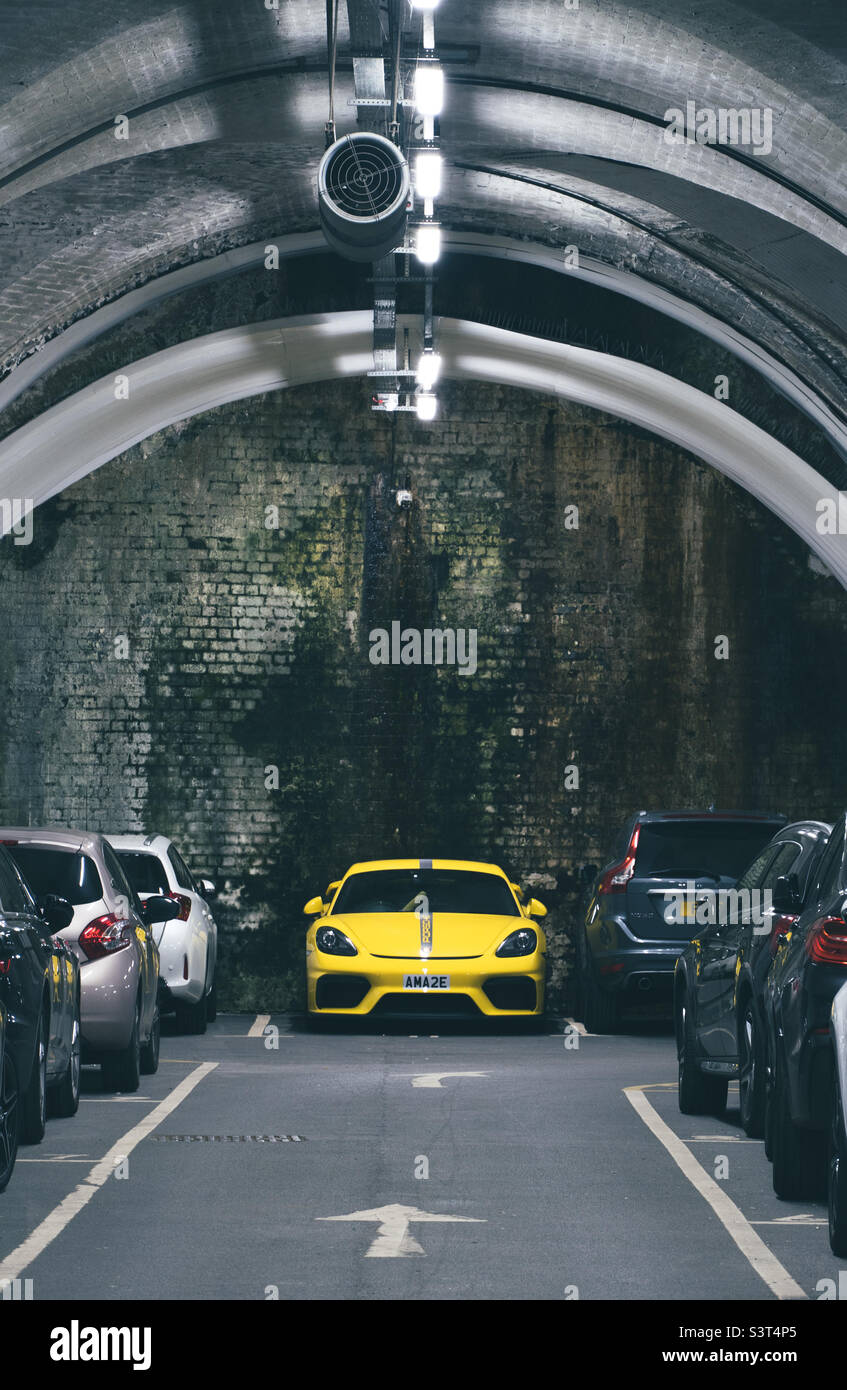 A dark underground car park or parking lot with rows of cars and a yellow sports car prominent Stock Photo