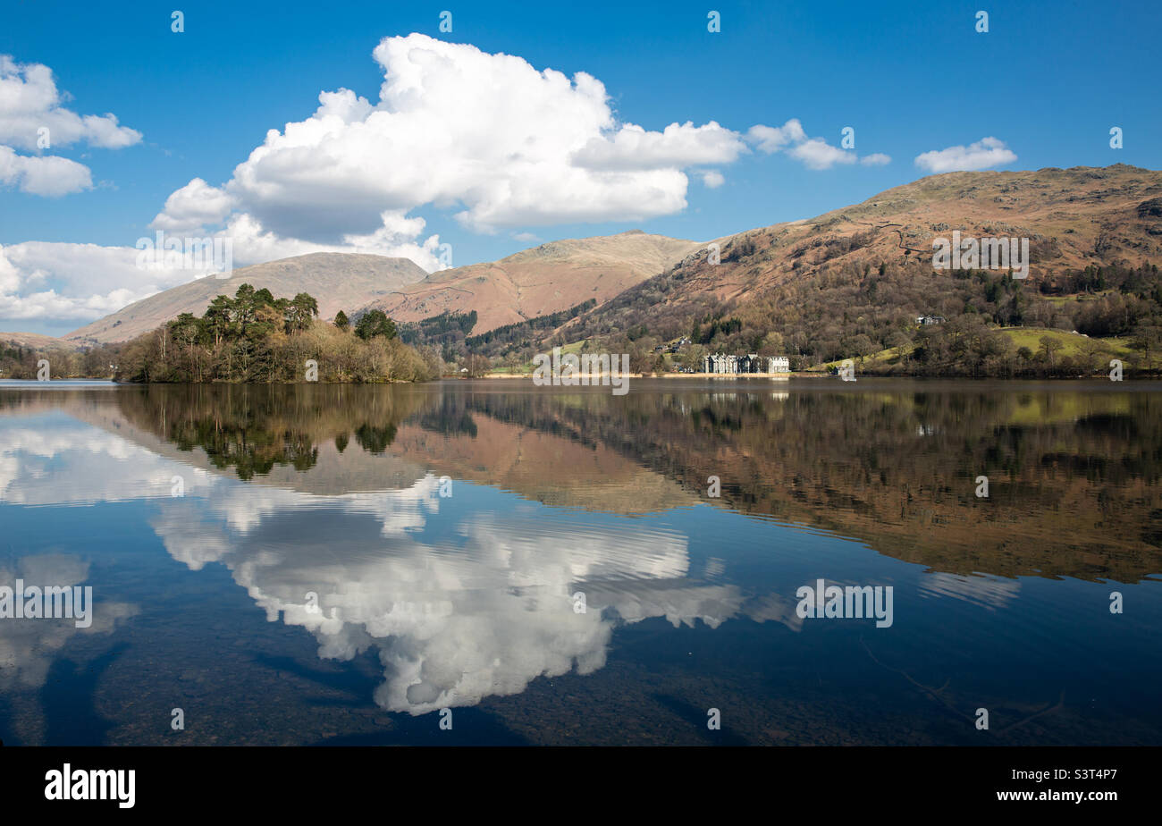 A picturesque and scenic landscape of Grassmere lake in Ambleside in the Lake District National Park with fluffy white clouds reflected in the calm waters and mountains and hills in the background - Smartphone Captured Stock Image