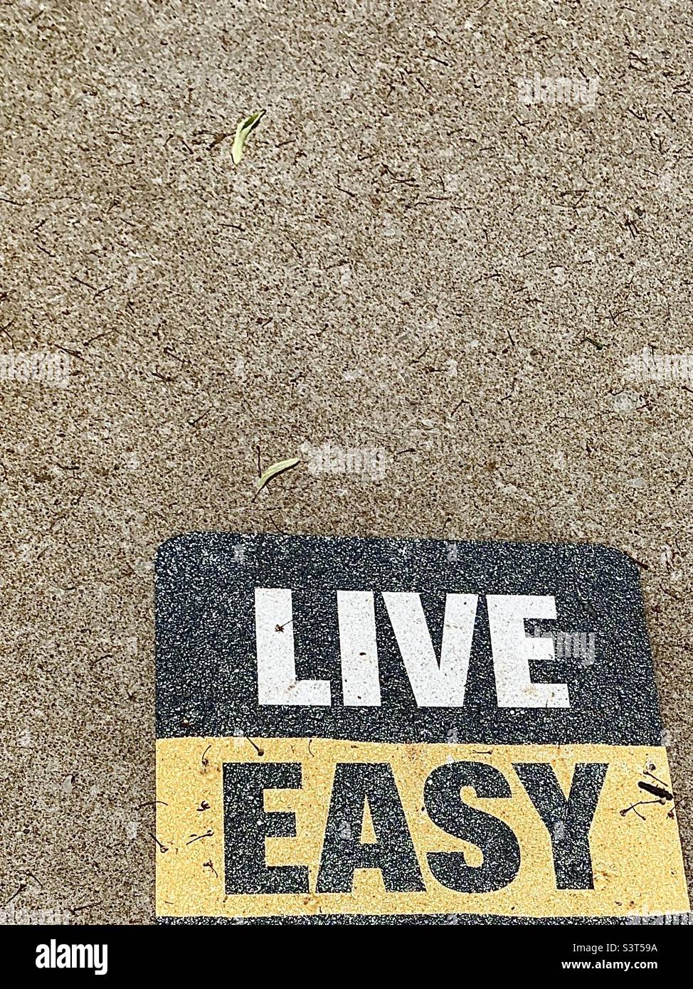 Black and yellow words painted on sidewalk, says LIVE EASY - Smartphone Captured Stock Image