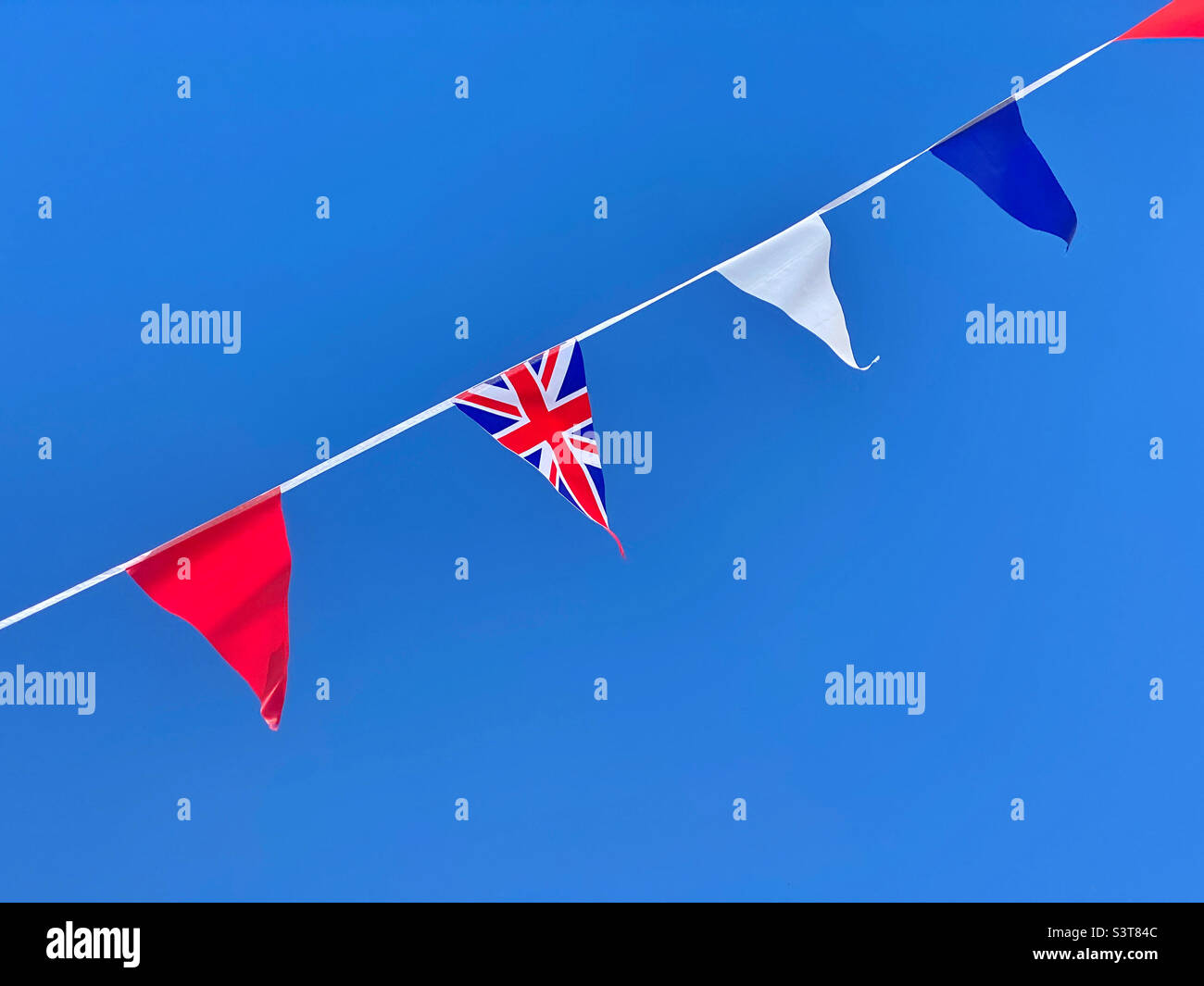 Red, white and blue bunting flutters in the wind alongside a Union Jack flag. This bunting was a part of the celebrations to mark the Queen’s Platinum Jubilee celebrations. Photo ©️ COLIN HOSKINS. - Smartphone Captured Stock Image
