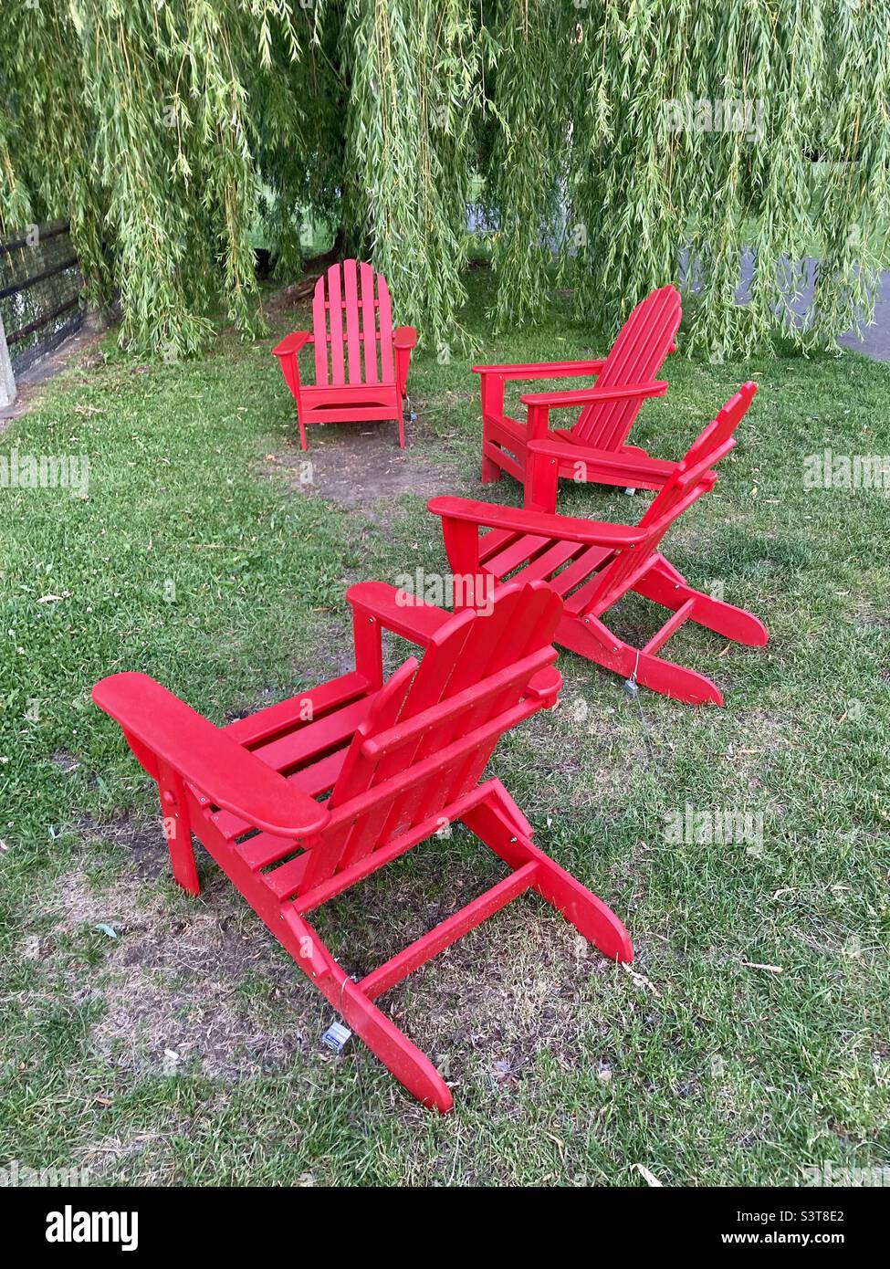 A foursome of red Muskoka chairs waiting for guest along Patterson Creek. - Smartphone Captured Stock Image
