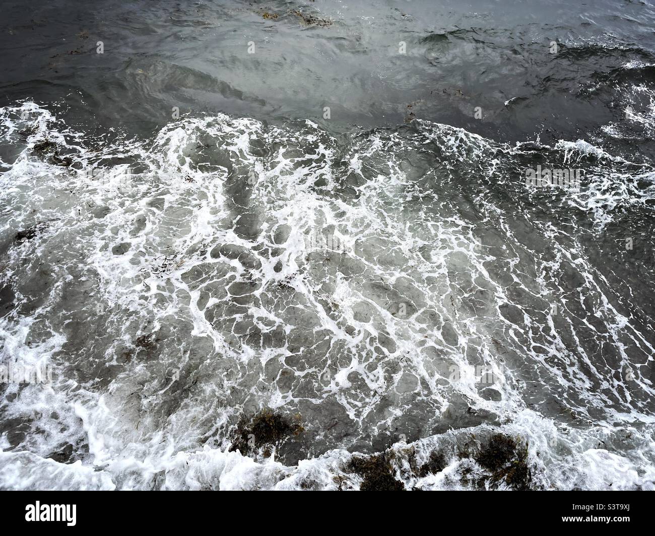 Looking down at the water on the seafront during summer in Oban, Scotland on a dull grey day. - Smartphone Captured Stock Image