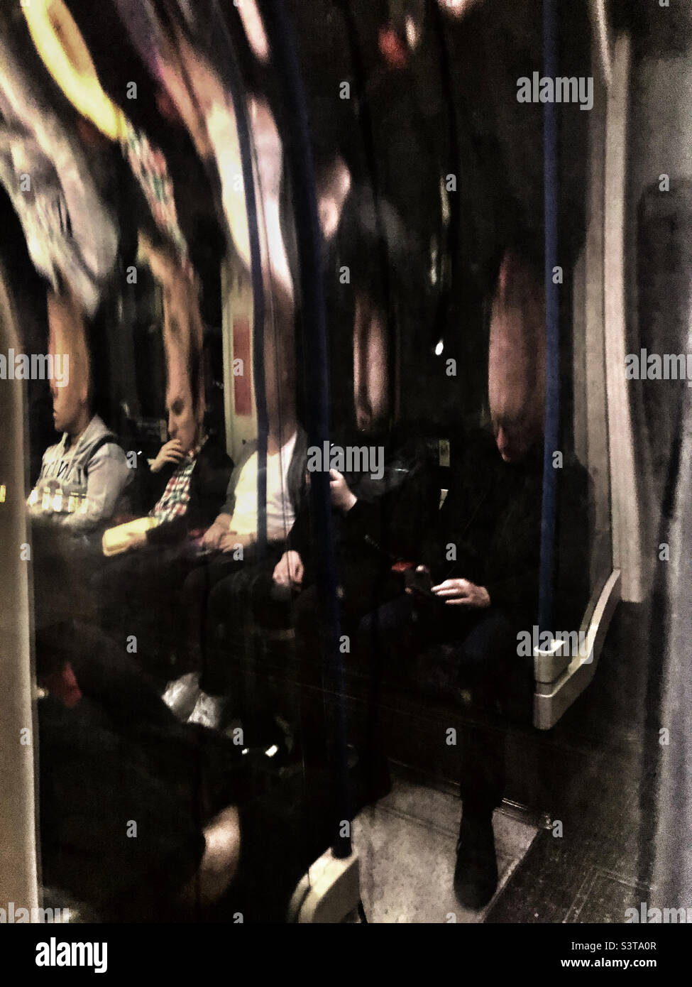 Commuters and their distorted reflections the curved  windows creating a  surreal scene on London Underground  train - Smartphone Captured Stock Image