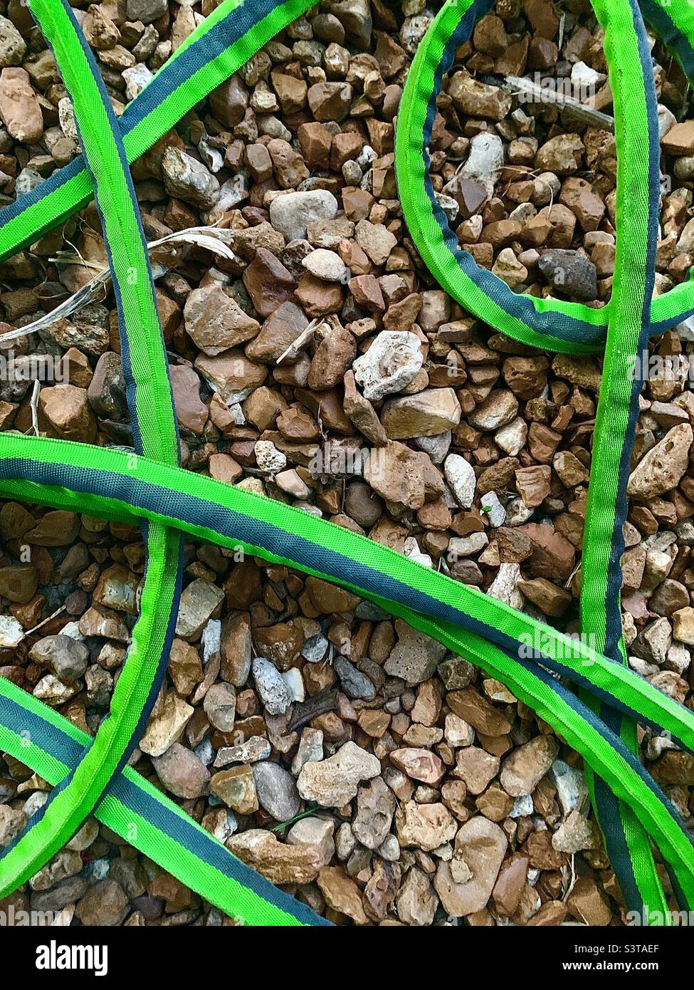 Vivid green garden hose on background of river rocks Stock Photo