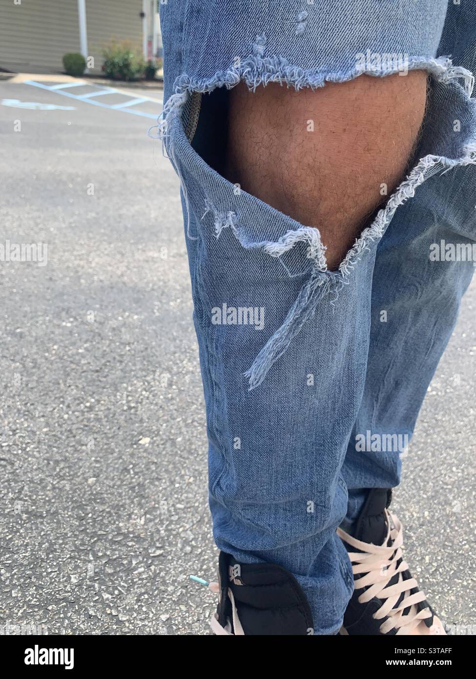 Mans legs wearing blue jeans with ripped knees Stock Photo