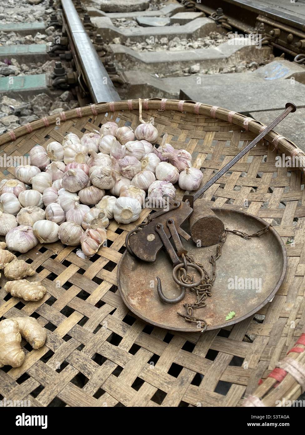Flat woven basket with garlic, ginger and old scales on a railroad tracks. Stock Photo