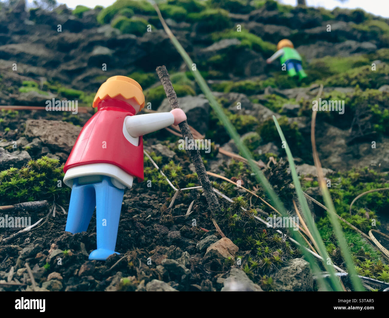 Low angle view of two toy figurines hiking uphill on a moss covered mountain in what appears to be an epic adventure - Smartphone Captured Stock Image