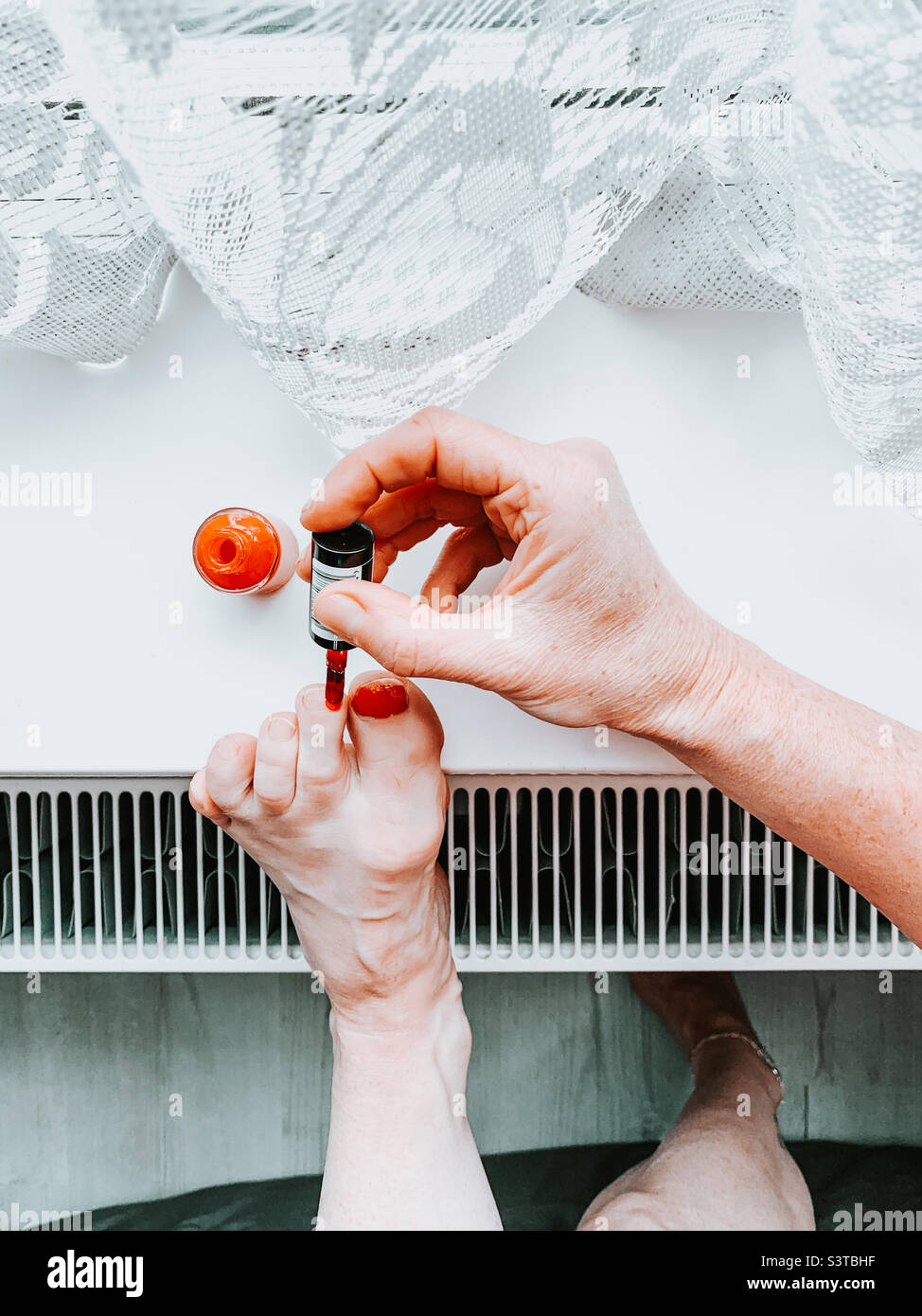 Woman painting her toenails red resting on the window sill - Smartphone Captured Stock Image