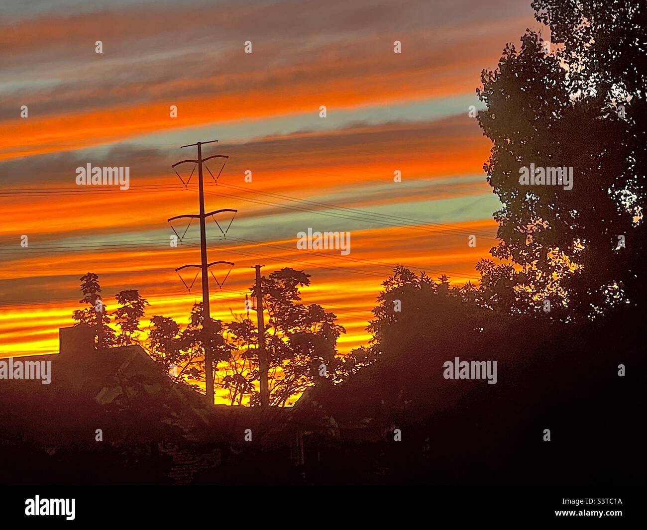 Summer sunset from a homes’ upstairs window in Utah, USA. The local Utah neighborhood is seen in silhouette against a radiant, glowing sky. - Smartphone Captured Stock Image