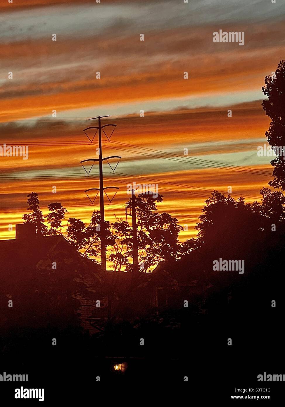 Summer sunset from a homes’ upstairs window in Utah, USA. The local Utah neighborhood is seen in silhouette against a radiant, glowing sky. - Smartphone Captured Stock Image