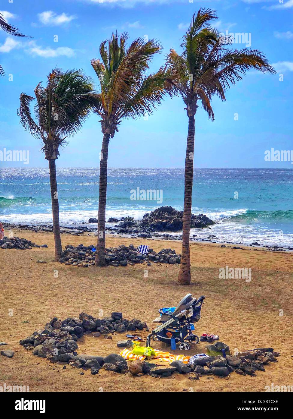 Pushchair inside a rock wind shelters around palm trees on Puerto del Carmen beach in Lanzarote, Canary islands, Spain. - Smartphone Captured Stock Image Pushchair inside a rock wind shelters around palm trees on Puerto del Carmen beach in Lanzarote, Canary islands, Spain. - Smartphone Captured Stock Image