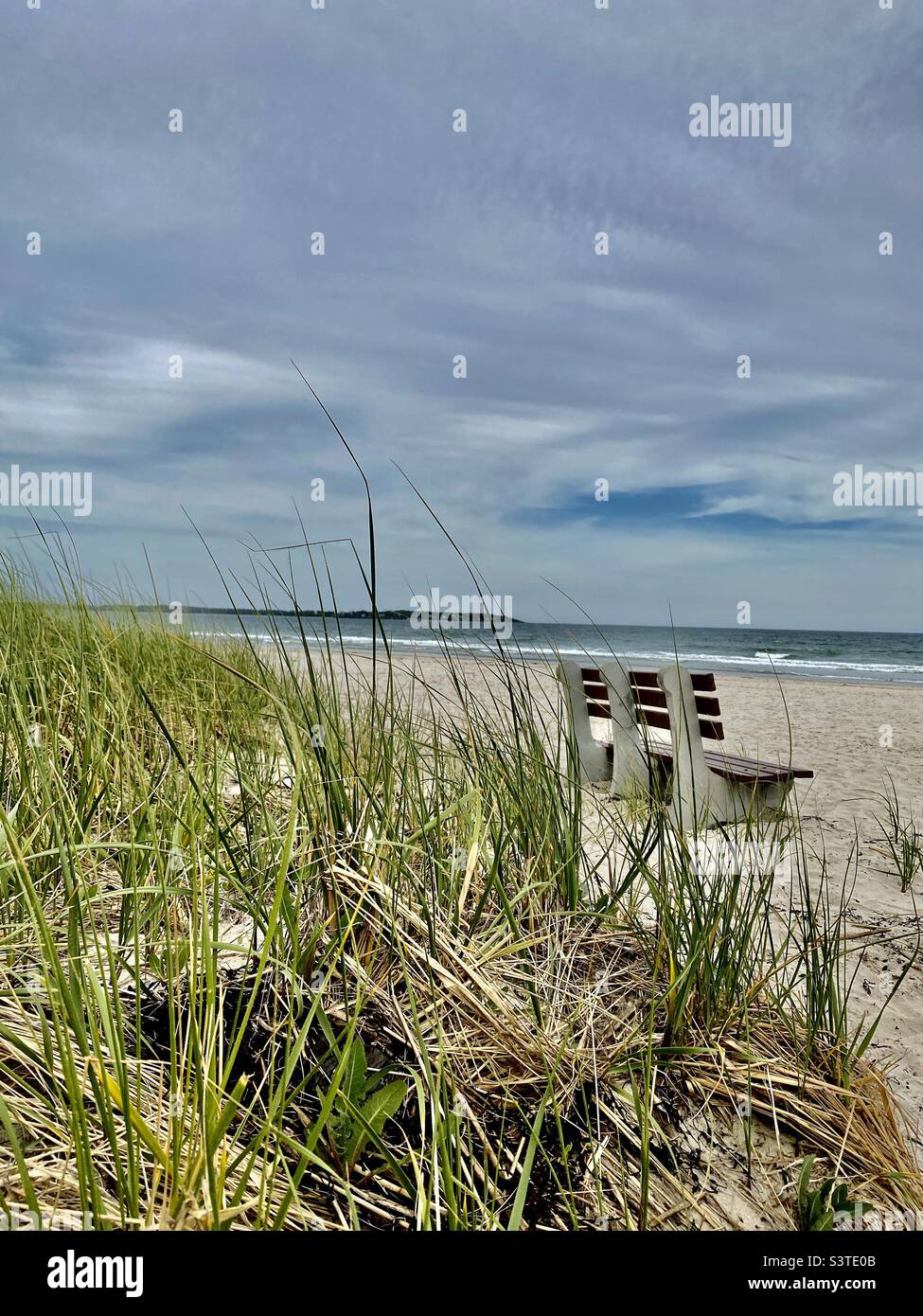 Old Orchard Beach, Maine. Serene scene looking through sea grass and an empty bench looking out at the ocean. - Smartphone Captured Stock Image