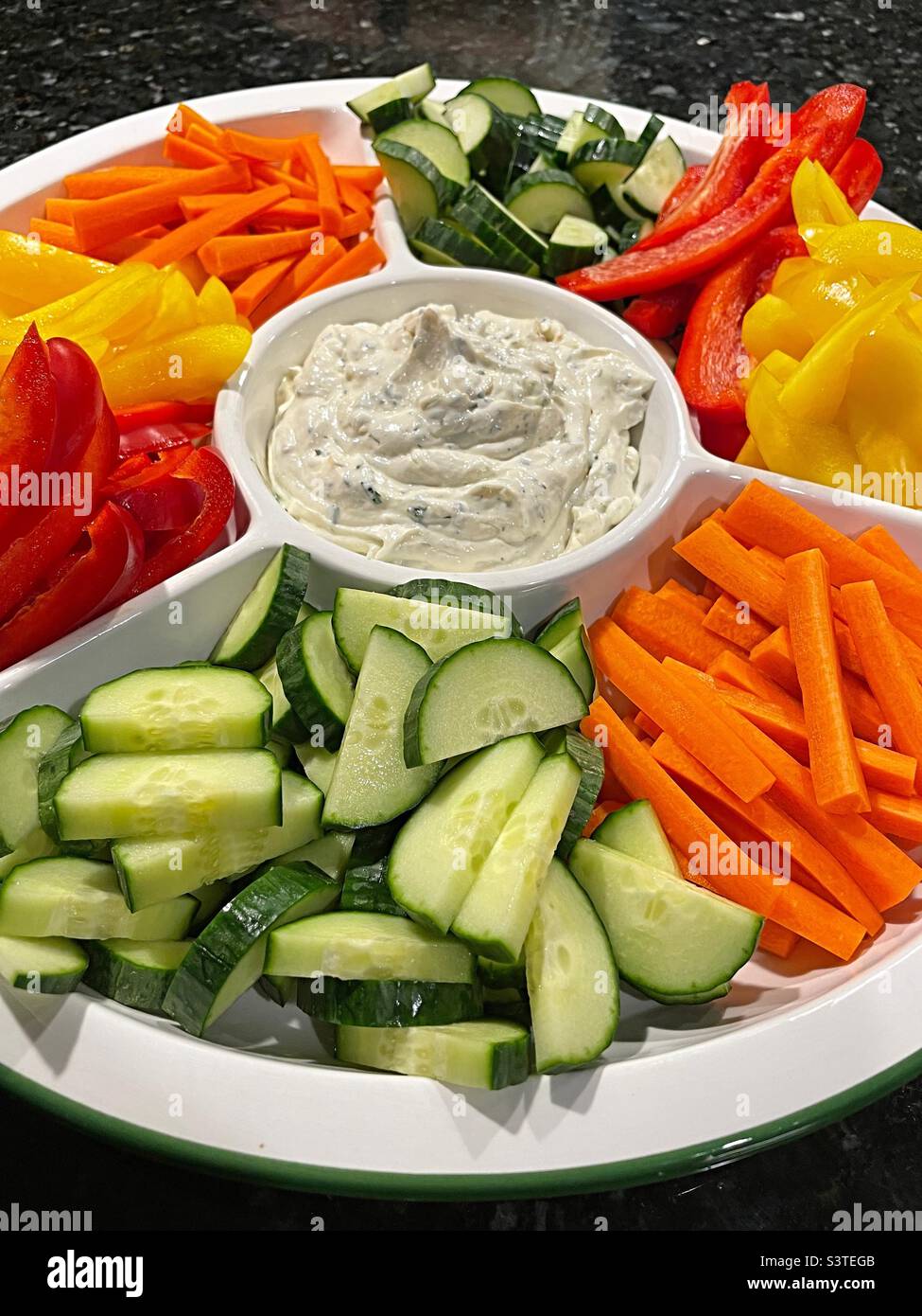 Close-up of a vegetable platter with freshly cut pieces of cucumbers, carrots, yellow peppers and red peppers surrounding a bowl of homemade dip, 2022, USA - Smartphone Captured Stock Image