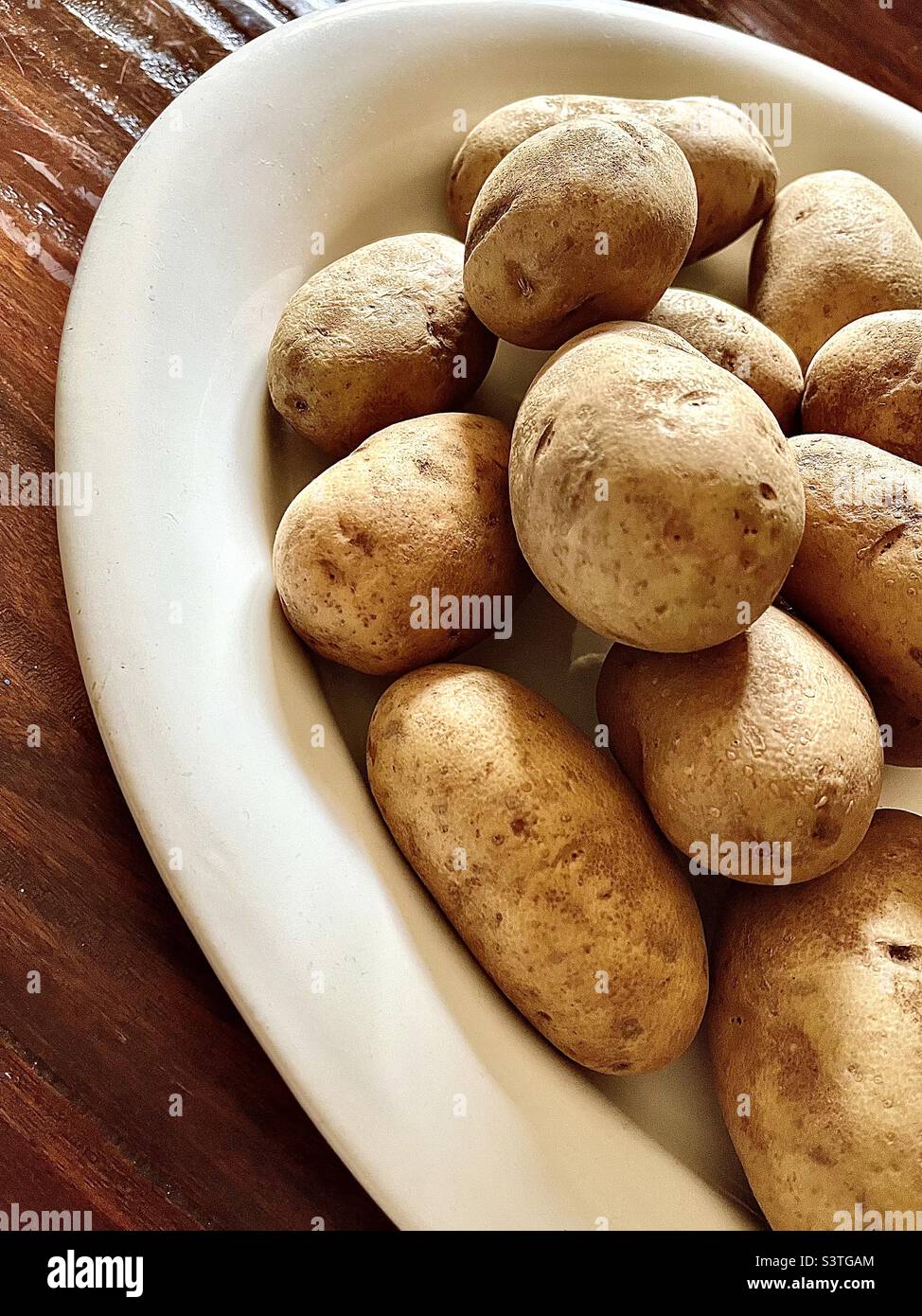 Big white plate of fresh, clean, potatoes on wooden table Stock Photo