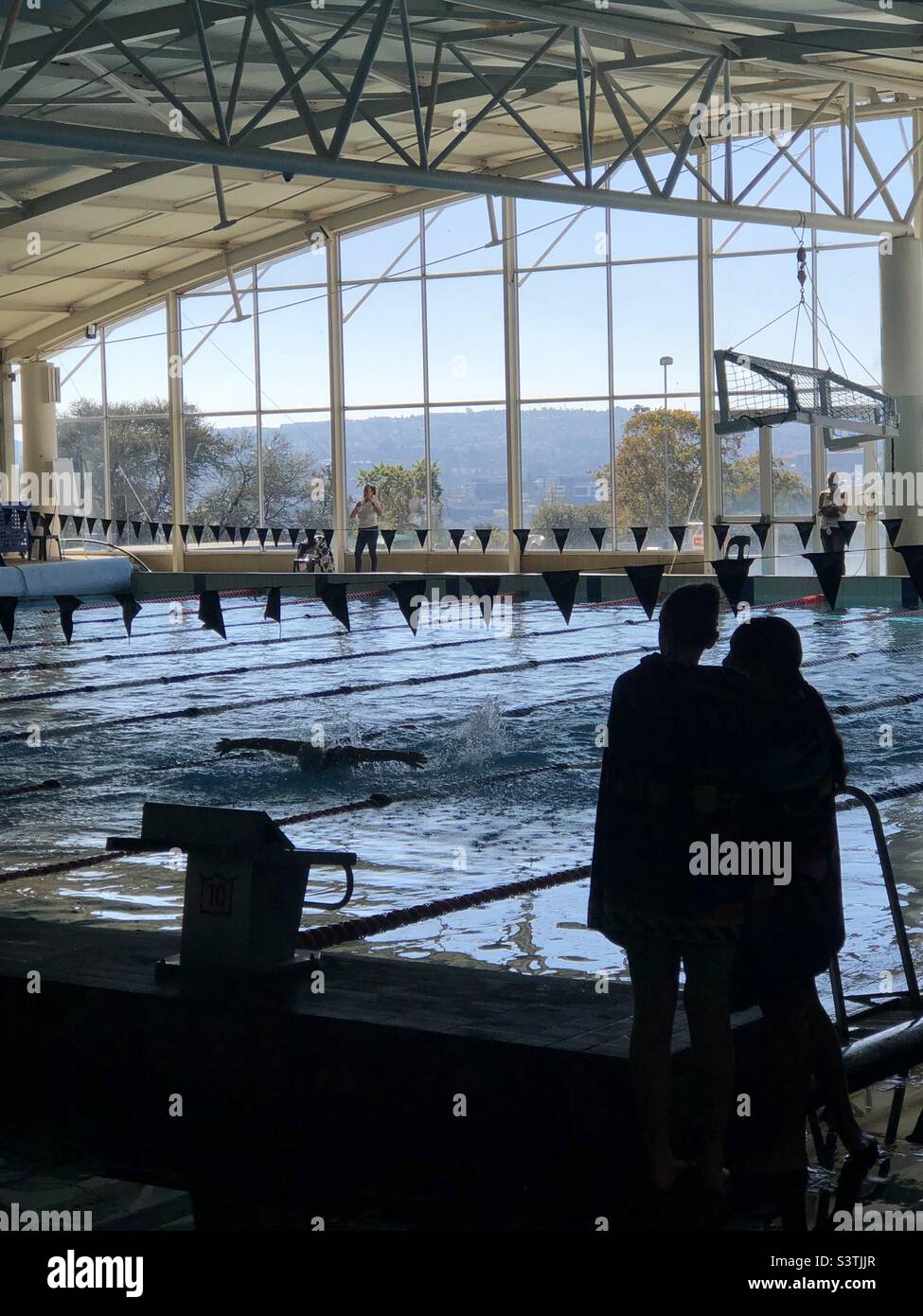 Swimmers watching a fellow swimmer doing butterfly at an indoor aquatics centre - Smartphone Captured Stock Image