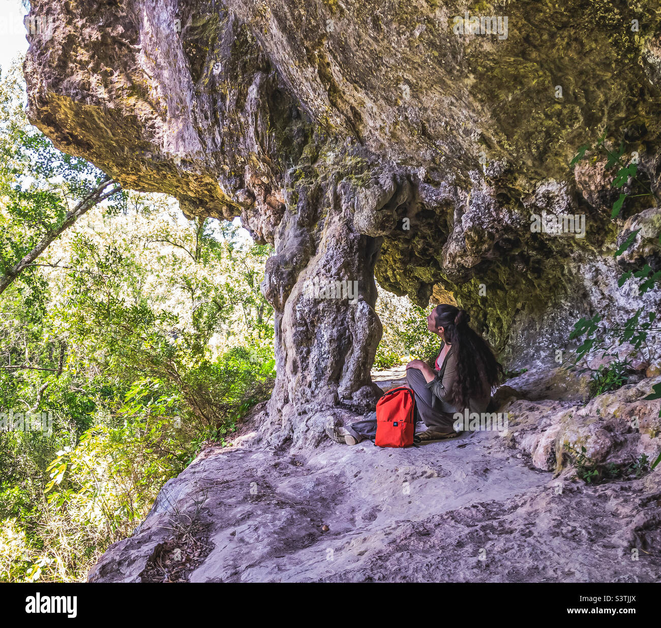 Female hiker sits beneath a natural archway on the edge of a cliff, at Lapas, Central Portugal - Smartphone Captured Stock Image