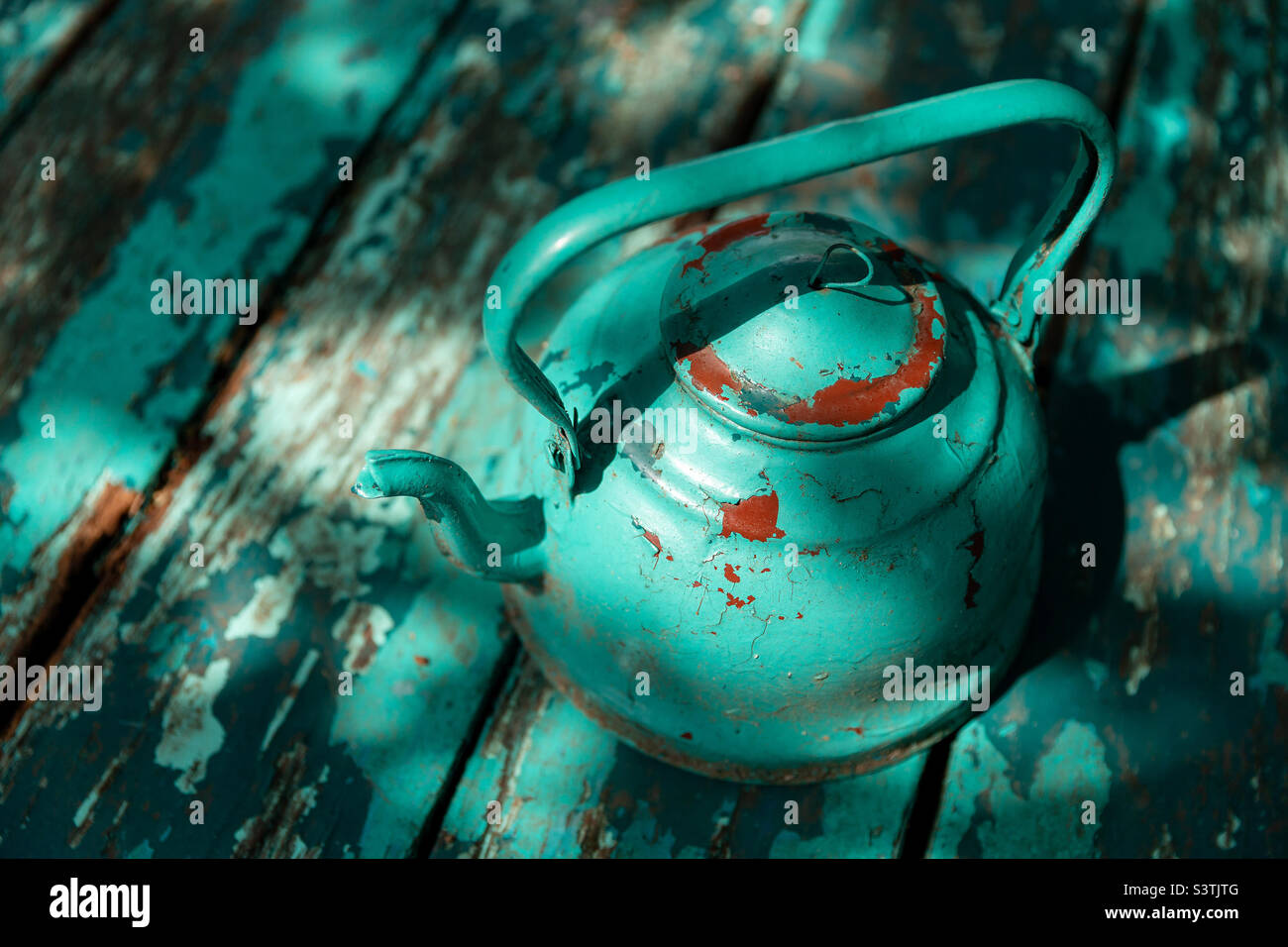 An old turquoise colored tea kettle on wooden grunge background, interesting shadows - Smartphone Captured Stock Image