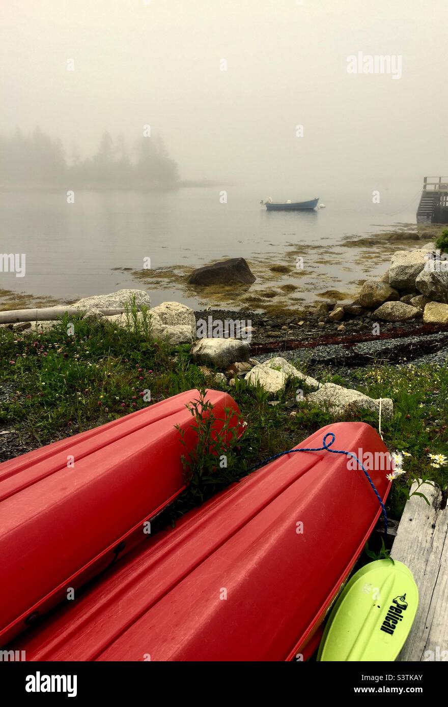 Fog rolls in. Kayaks on the shore, boat in the water. A sheltered cove in the Atlantic Ocean, Halifax, Canada. Stock Photo